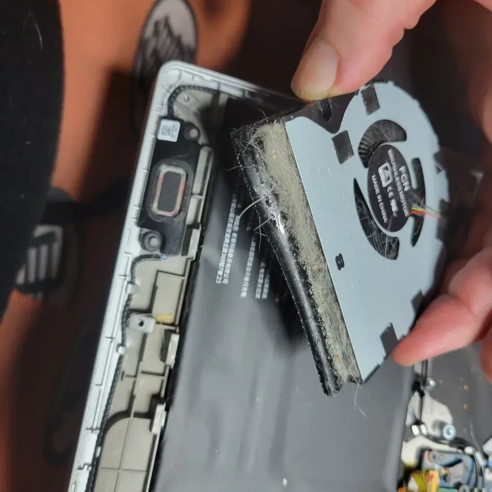 Close-up of a person removing a dusty and hairy internal component from a disassembled electronic device, possibly a smartphone or similar gadget.