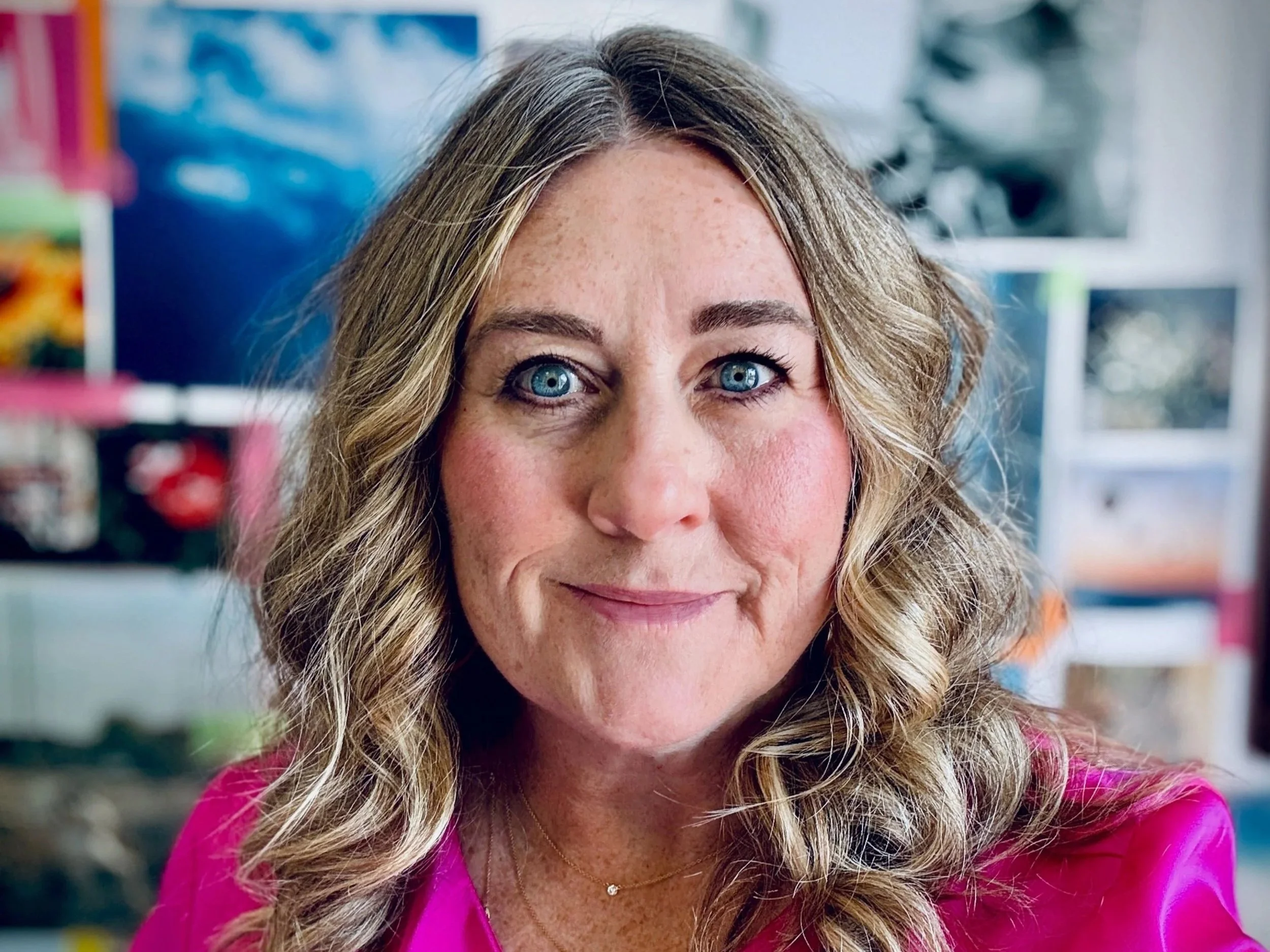 Self portrait of Sarah Beckman, creative strategist, miling in a bright pink blouse in front of a colorful blurred background