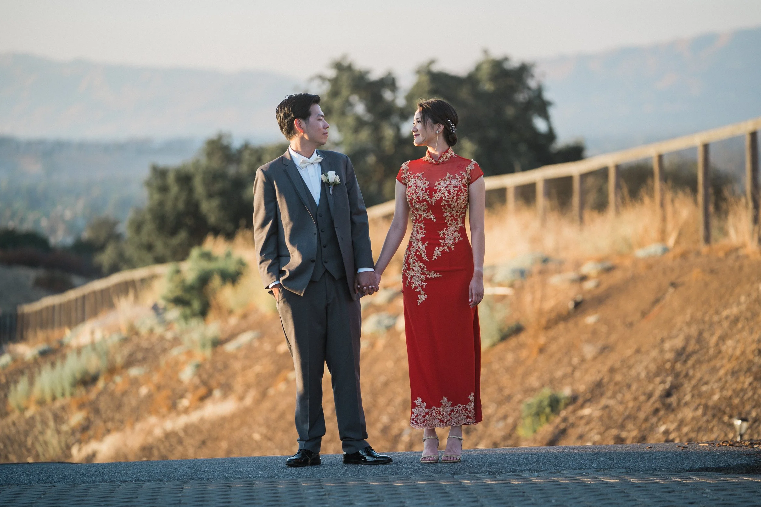 Newlyweds holding hands against scenic rolling hills during an outdoor wedding portrait session in California.
