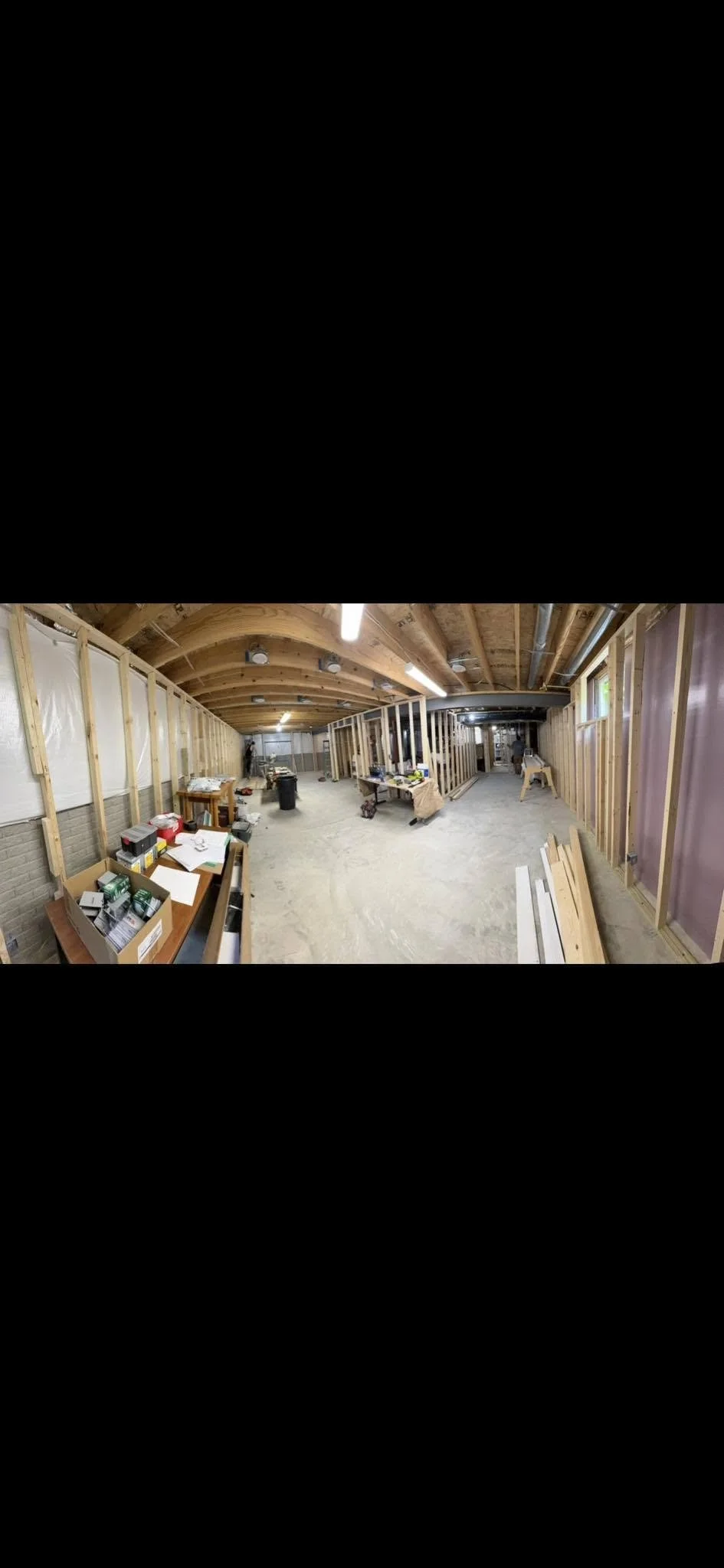 Interior view of a building under construction with exposed wooden framing, unfinished walls, and construction tools and materials scattered around