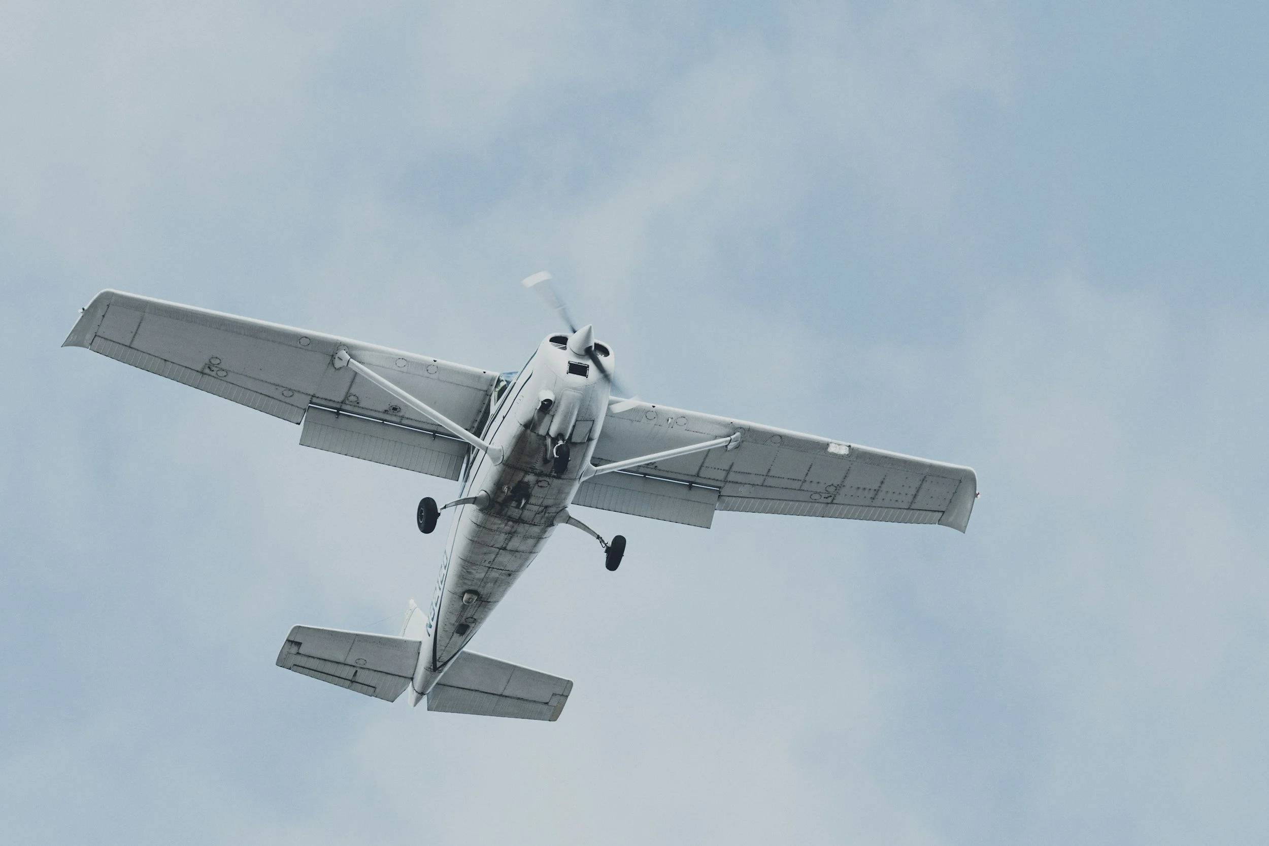 A small white airplane flying in a light blue sky.