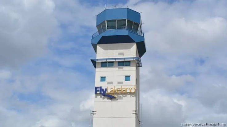 Air traffic control tower with a white base and blue top, cloudy sky background.