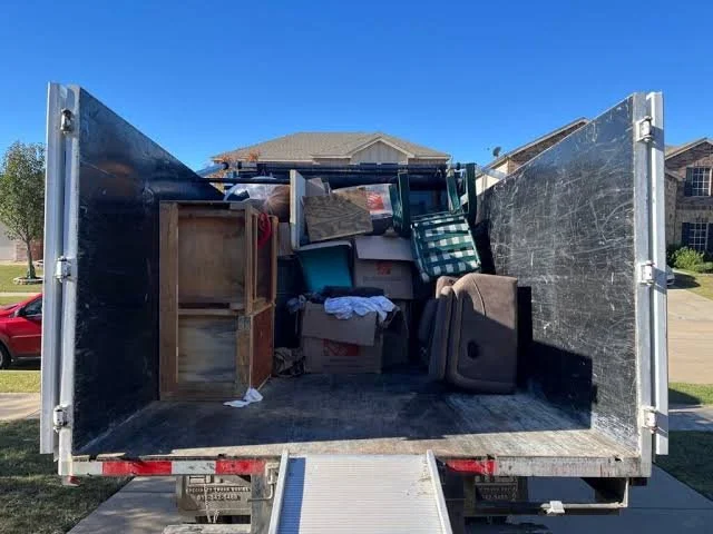 Open moving truck filled with furniture and boxes, parked in a residential neighborhood.