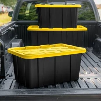 Three black storage containers with yellow lids stacked in the bed of a pickup truck.