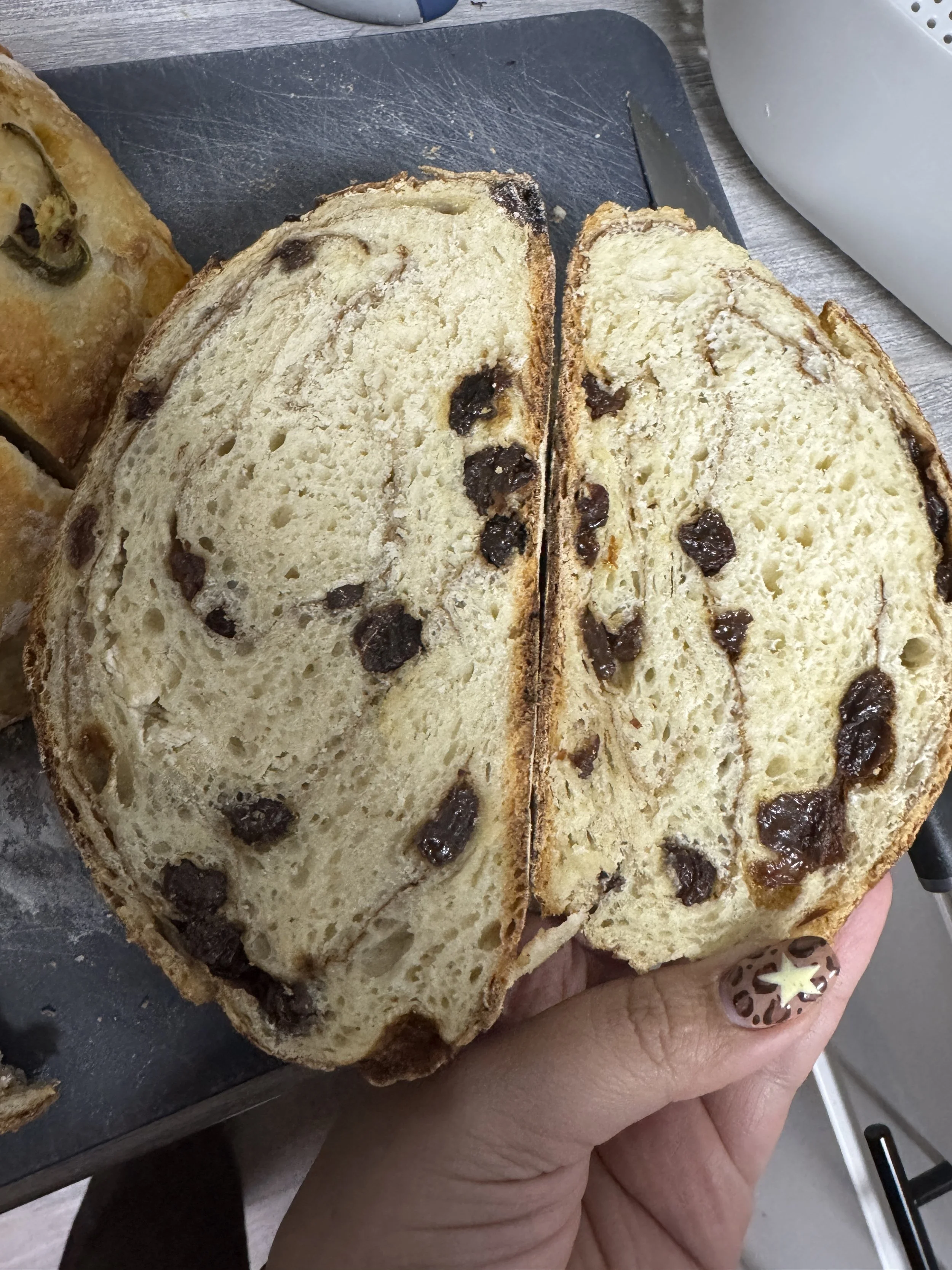 Close-up of a hand holding a slice of chocolate chip bread with a light crust and soft interior, on a gray surface.