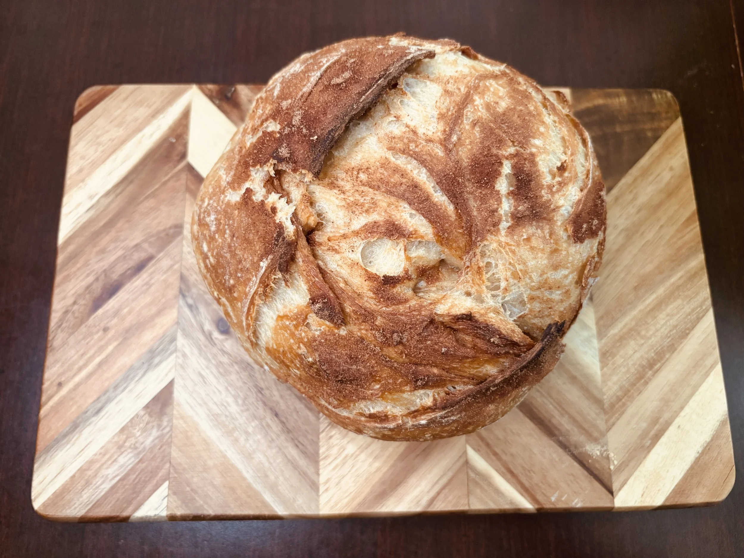 A round loaf of bread,
, with a crusty, golden-brown exterior, resting on a wooden cutting board