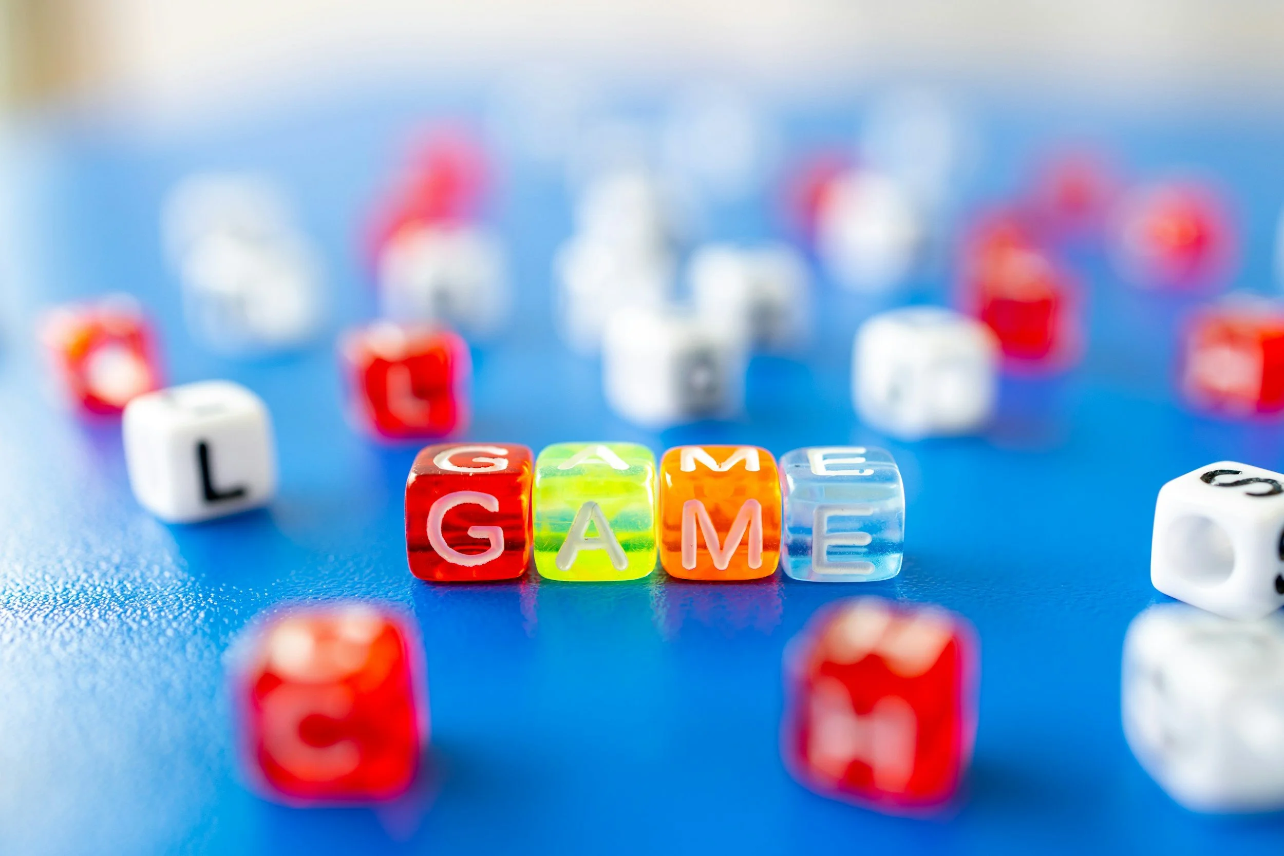 Colorful transparent game dice spelling out the word 'GAME' on a blue surface.