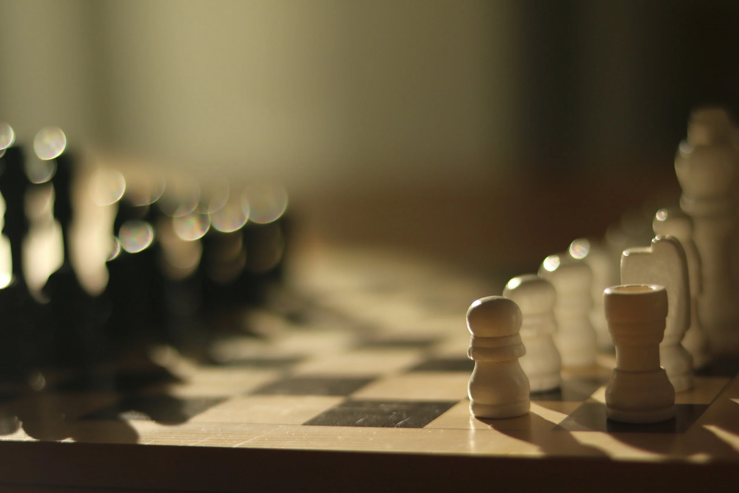 Close-up of a chessboard with white and black chess pieces set up for a game, with a focus on the white pieces in the foreground.