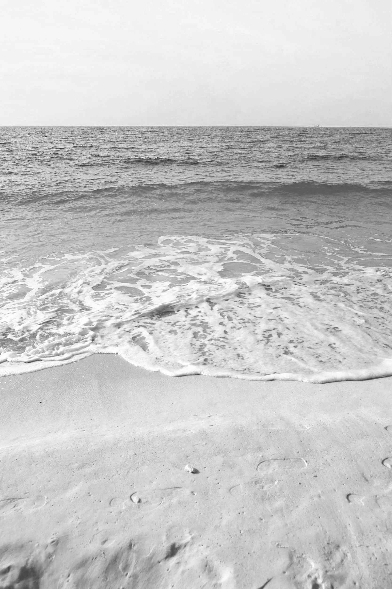 Black and white photo of a sandy beach with gentle waves, indicating calm and clarity.