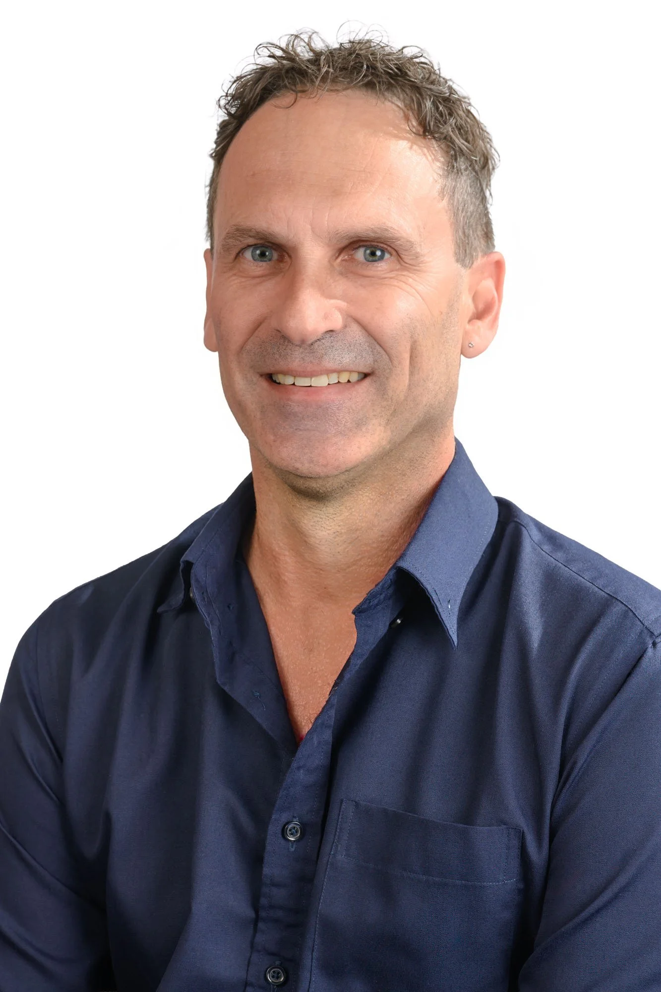 Close-up of smiling man with short, curly hair, wearing a dark blue button-up shirt, against a white background.
