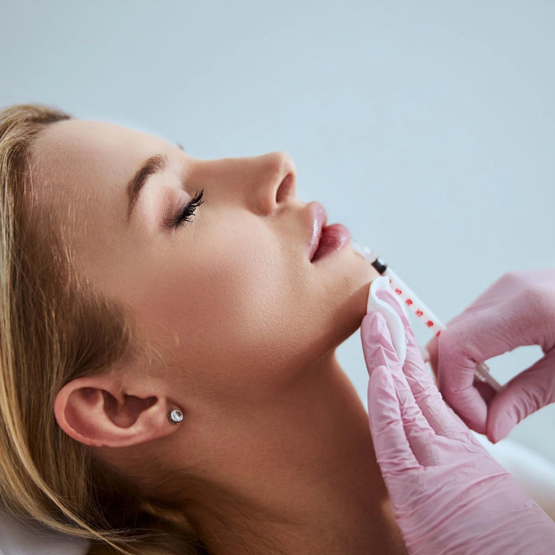 Mujer con oreja con pendientes, recibiendo una inyección en el brazo, vista lateral y en primer plano.
