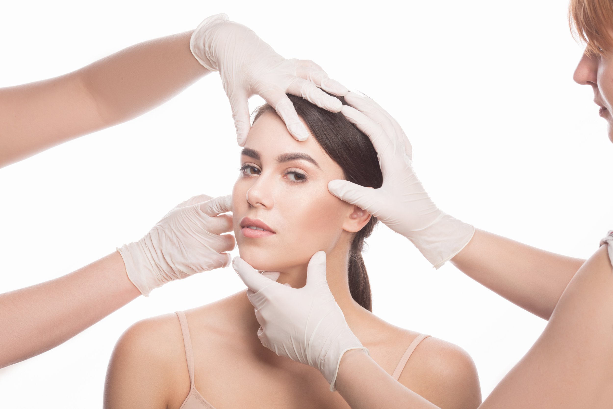 Mujer recibiendo una revisión estética facial por parte de personal médico con guantes.