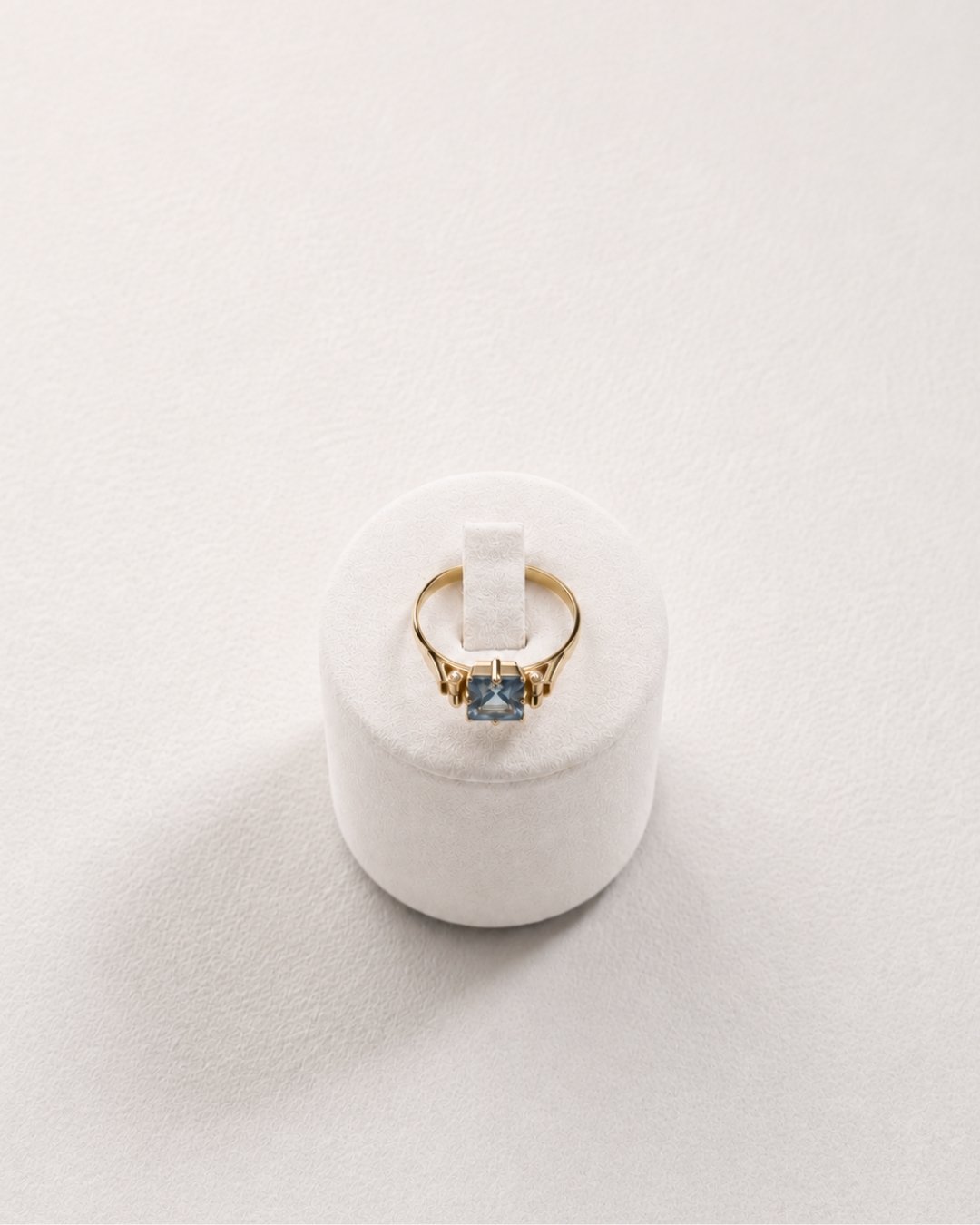 Front view of the gold ring with a blue topaz gemstone and side accent stones on a white ring stand