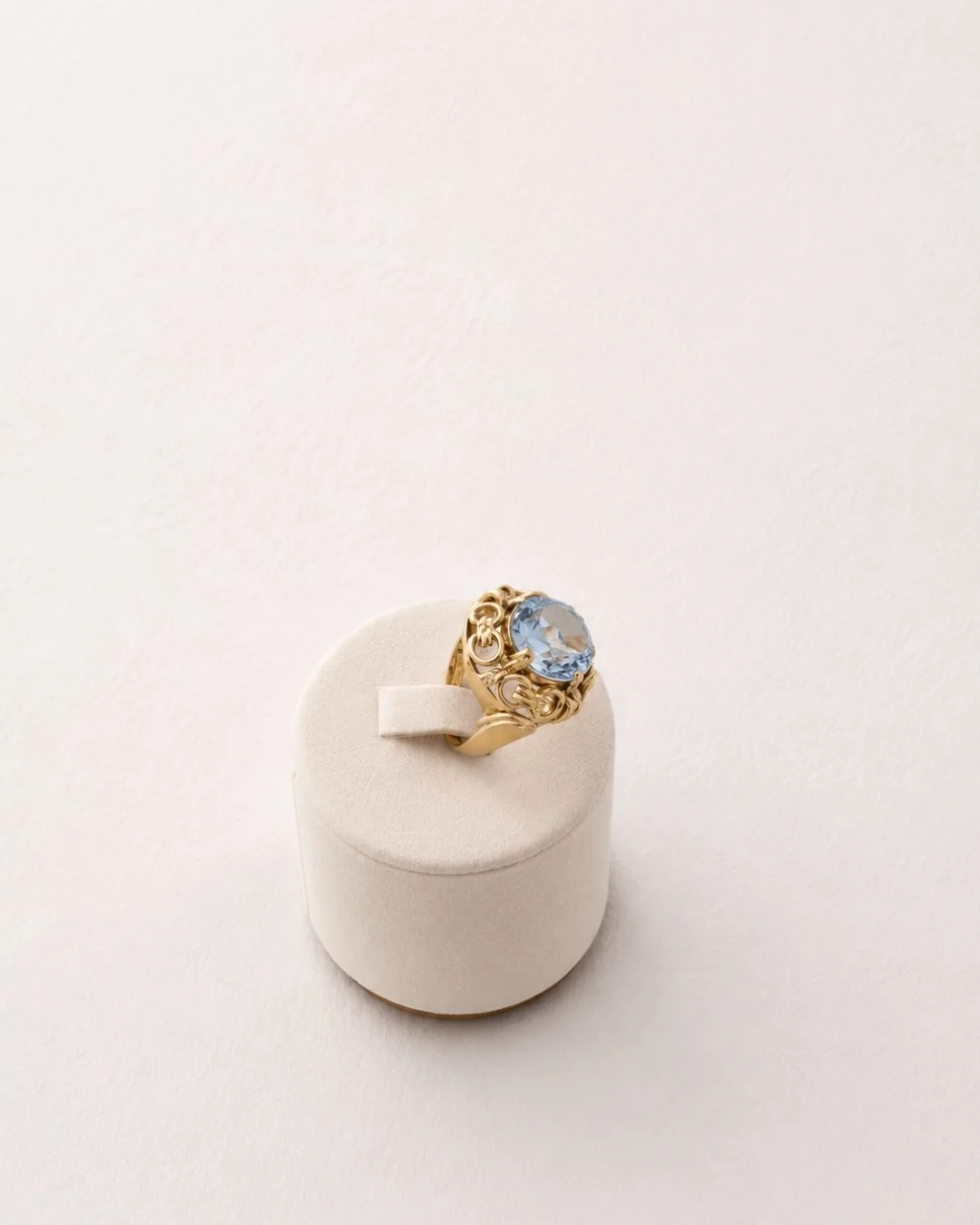 Angled view of the ornate gold cocktail ring with blue gemstone on a white ring stand