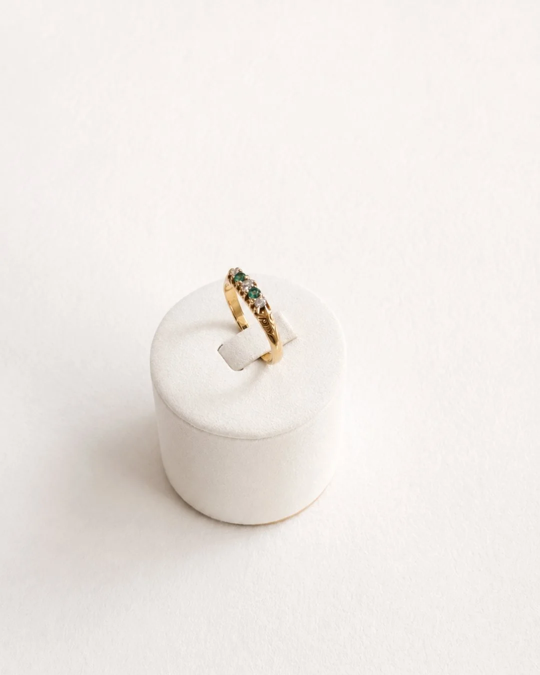Top-down view of the gold curved band ring with diamond and emerald accents on a white ring stand