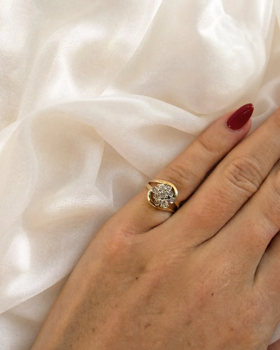 Close-up of a model wearing a vintage gold diamond cluster ring, shown on her hand against ivory fabric