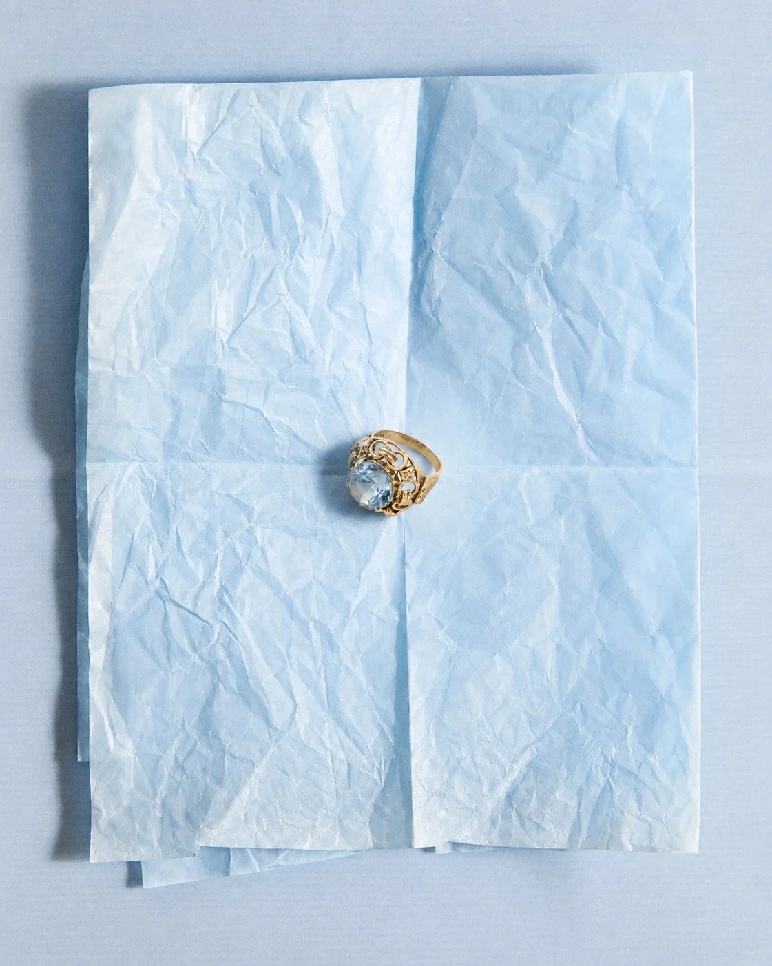 A large gold ring with a clear gemstone on a crumpled sheet of white tissue paper