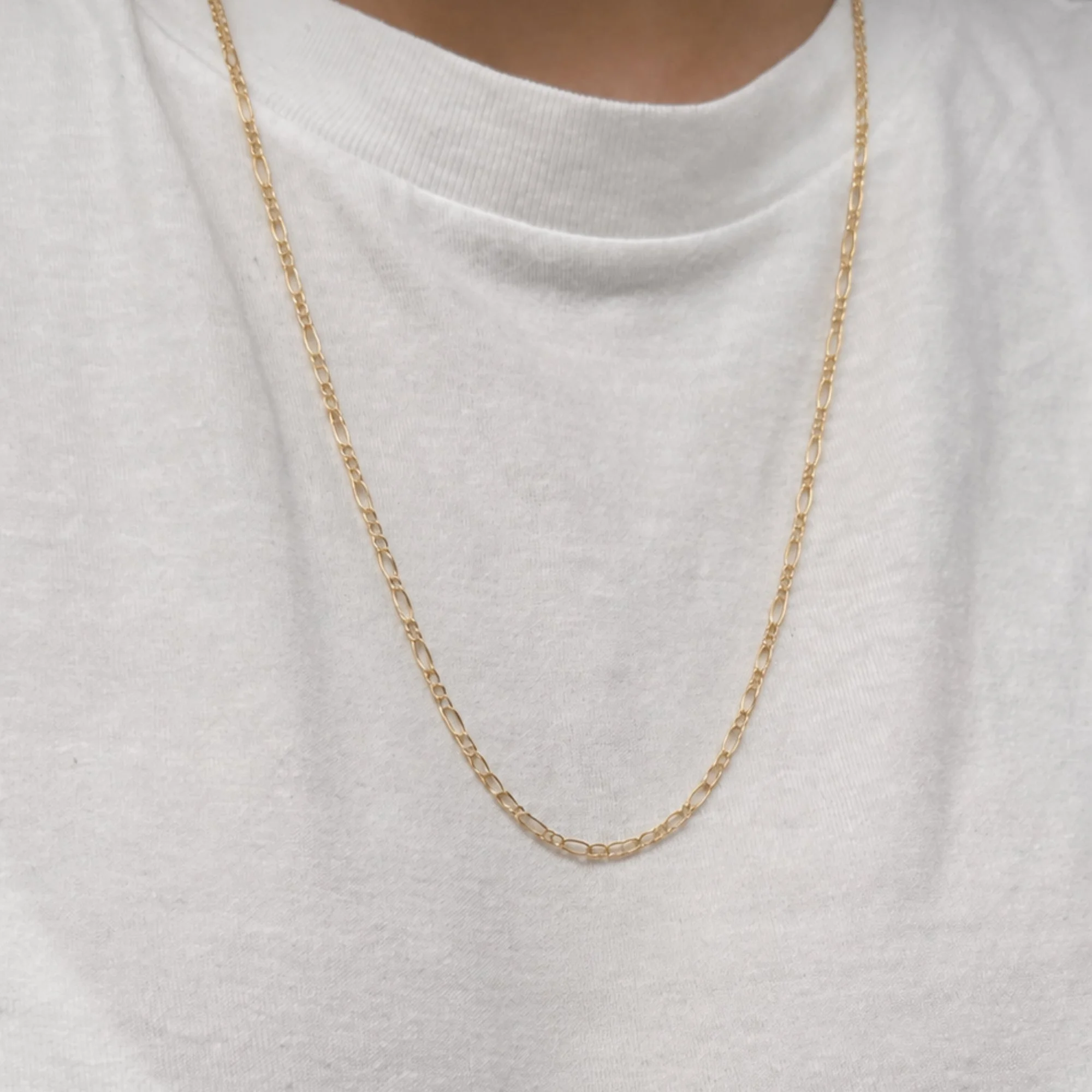 Close-up of a gold chain necklace hanging over a white shirt.