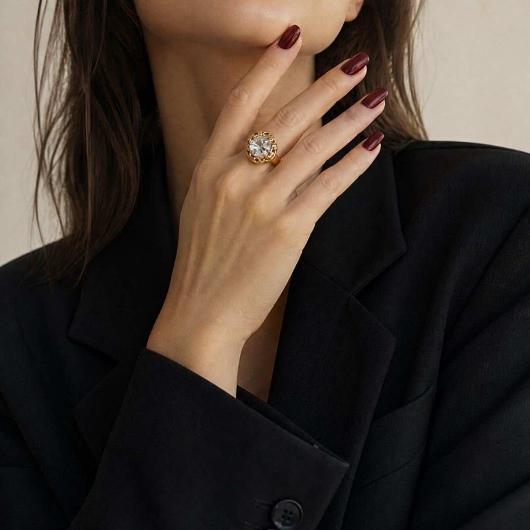 A woman modelling a vintage gold cocktail ring with a large clear gemstone, paired with a black blazer — a pre-loved piece from Vallora Vintage.