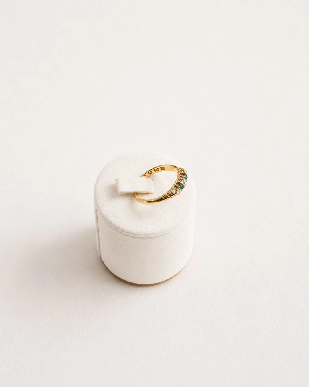 Angled view of the gold curved band ring with diamond and emerald accents on a white ring stand