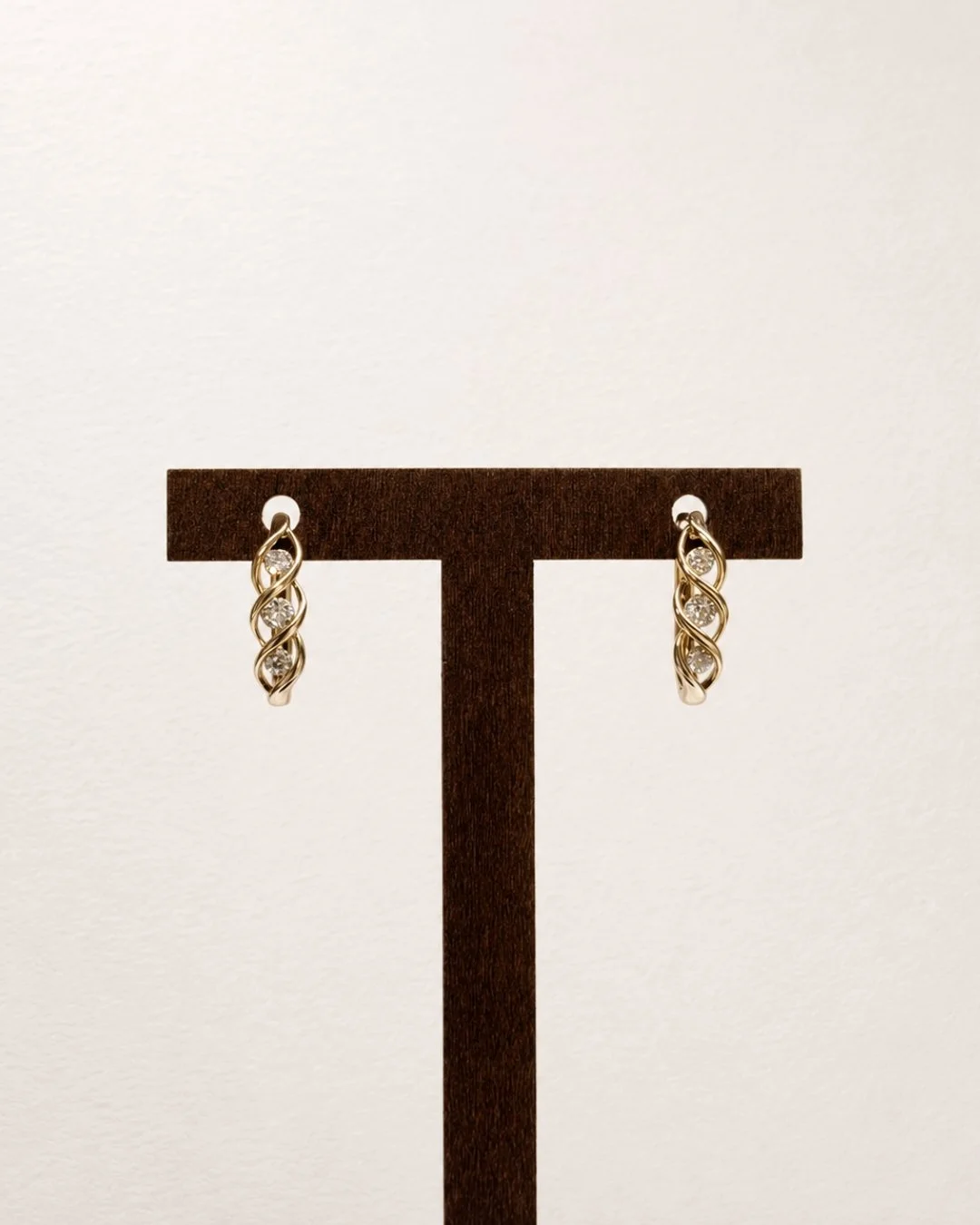 Gold twist huggie earrings with crystal accents displayed on a dark wood T-bar earring stand