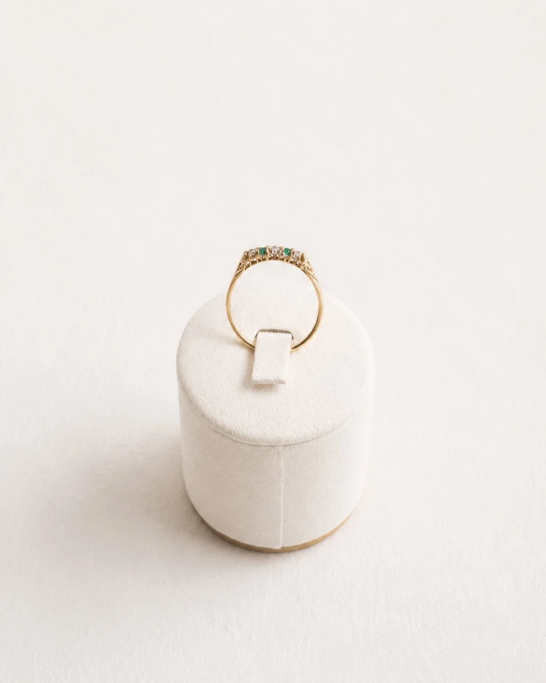 Front view of the gold curved band ring with diamond and emerald accents on a white ring stand