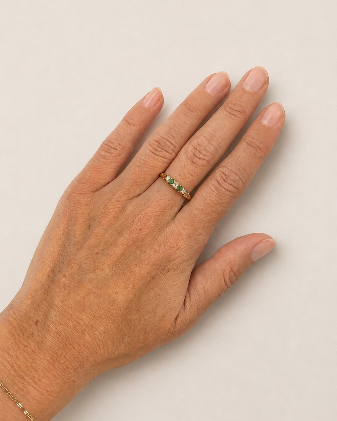 Close-up of a model wearing the gold diamond and emerald ring on her hand