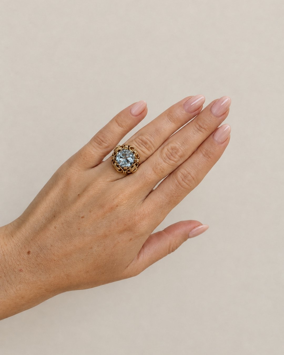 Model's hand fanned out wearing the ornate gold cocktail ring with a blue gemstone