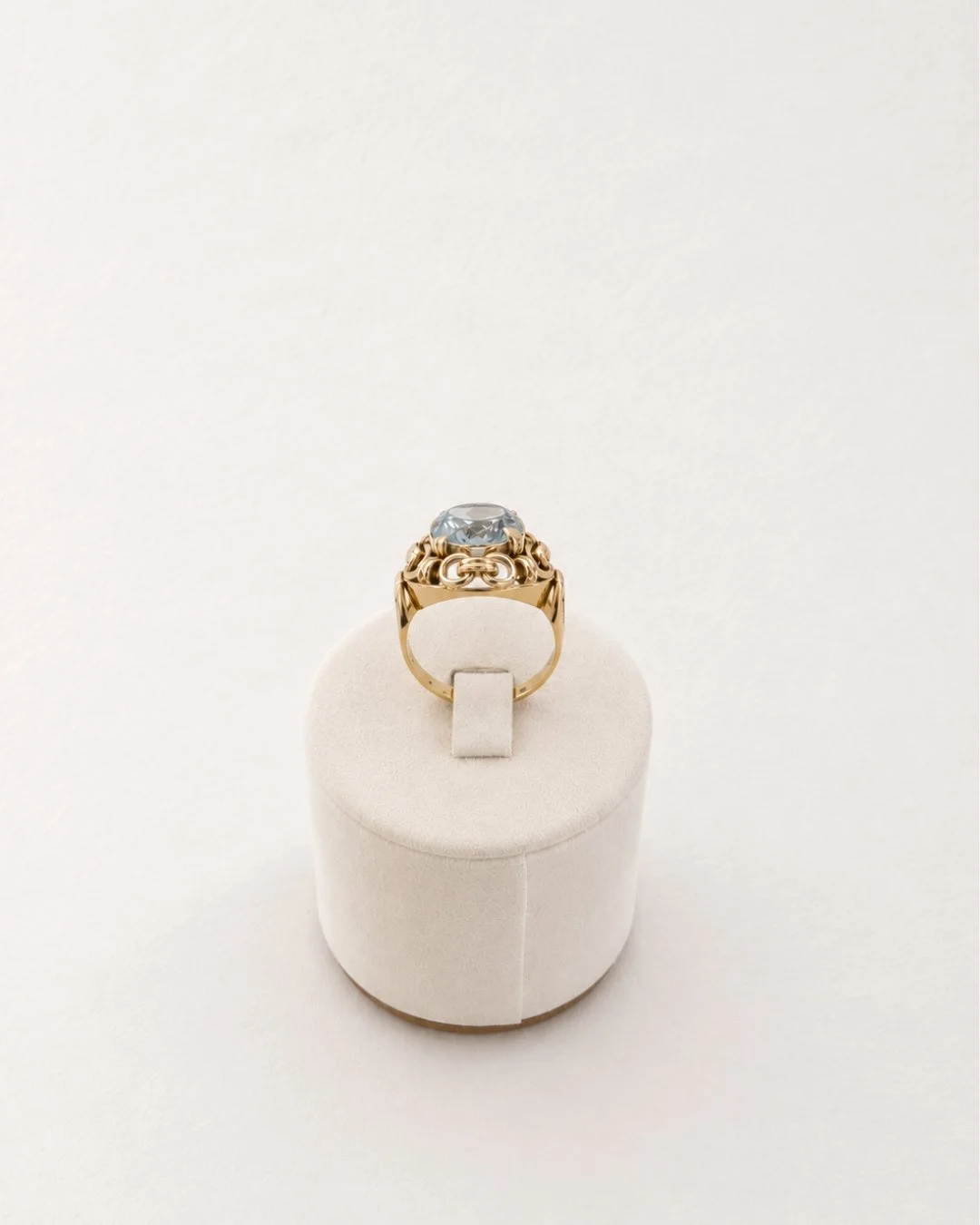 Ornate gold cocktail ring with a blue gemstone displayed on a white ring stand