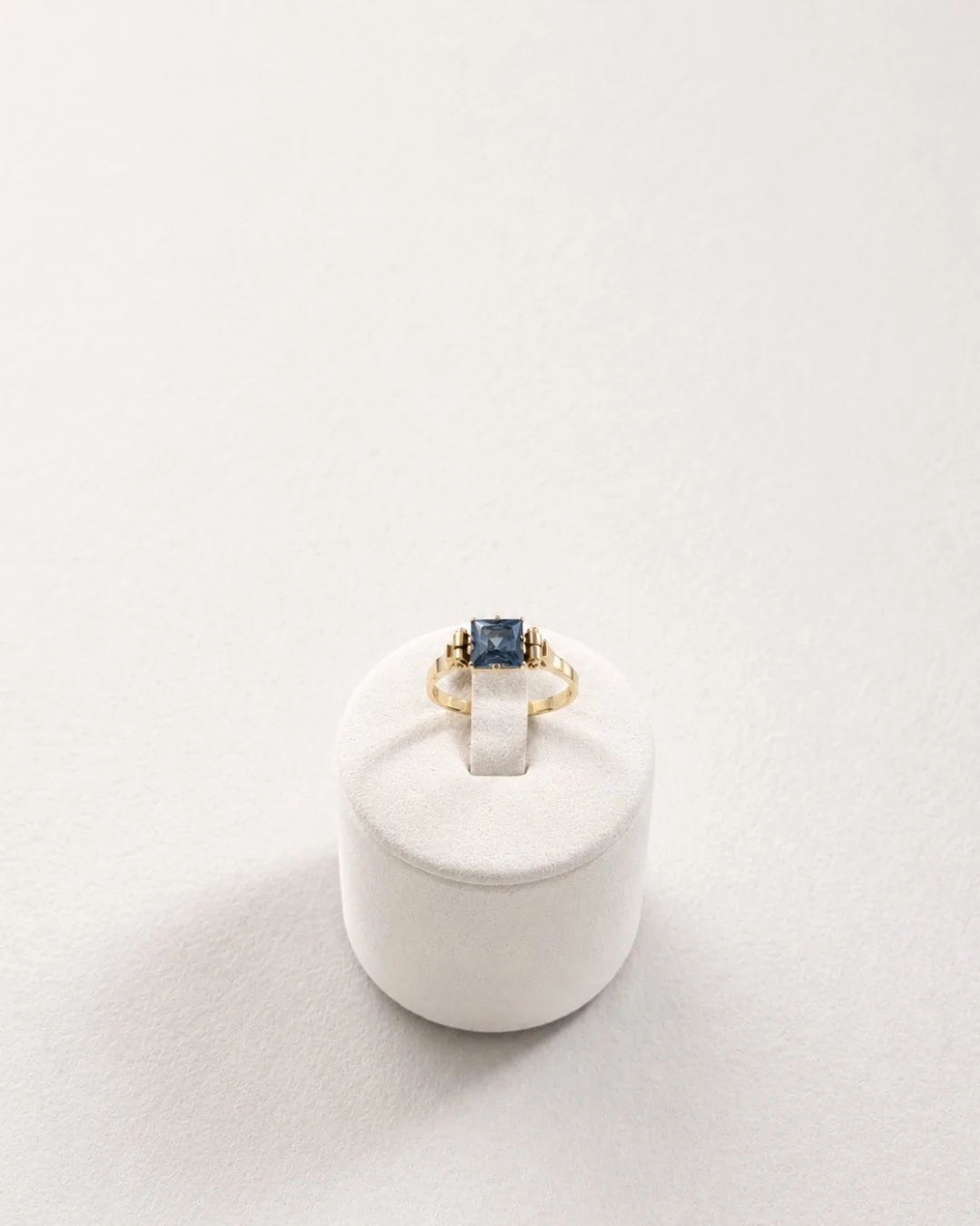 Angled view of the gold ring with blue topaz gemstone on a white ring stand