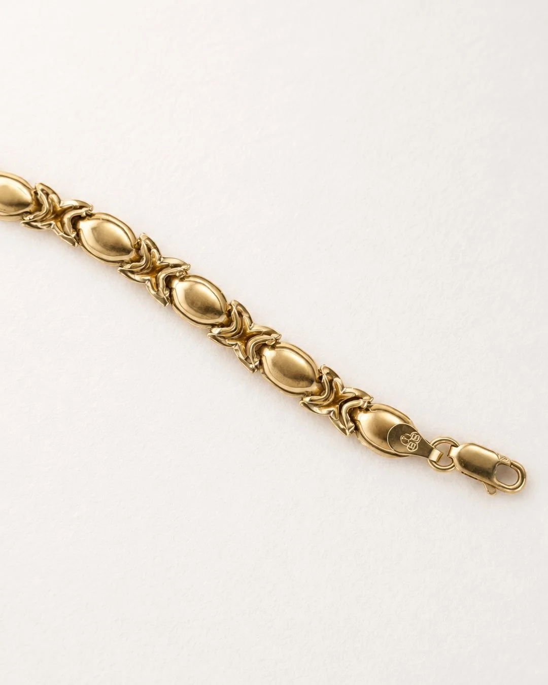Solid gold chain bracelet with decorative link design and clasp laid flat on a cream background