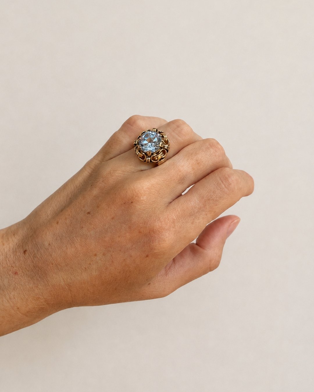 Close-up of a model wearing the ornate gold cocktail ring with a blue gemstone on her hand