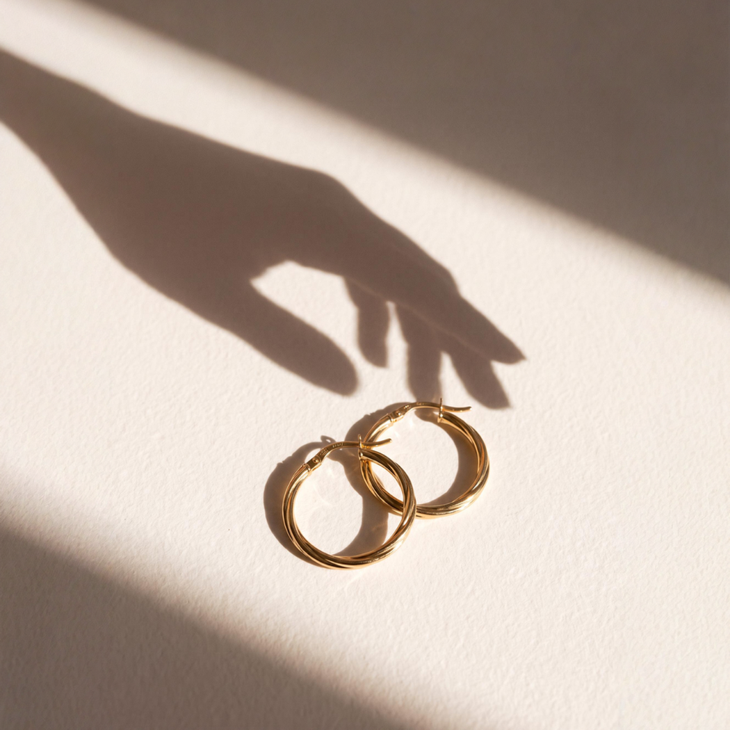 A pair of gold hoop earrings on a white surface with their shadows cast by sunlight.