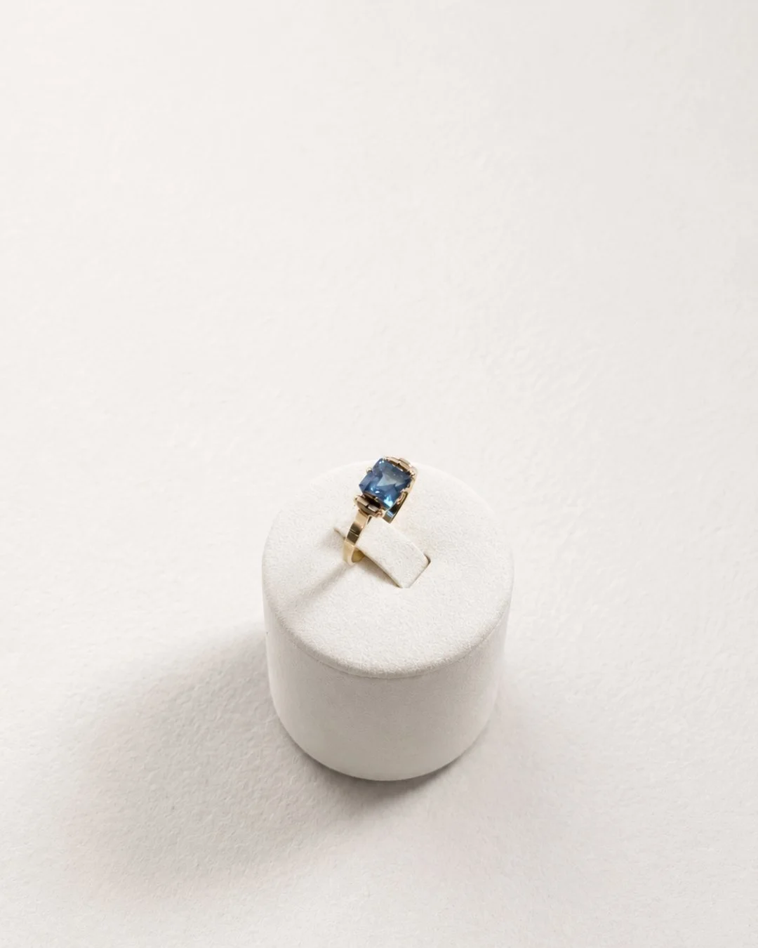 Gold ring with a blue topaz gemstone displayed on a white ring stand
