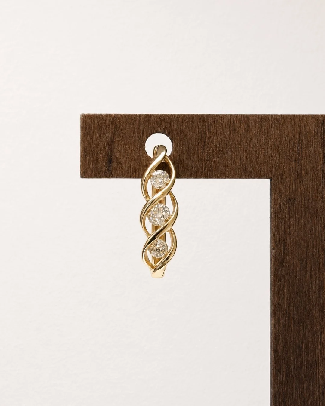 Macro close-up of a single gold twist huggie earring with pave crystal detail hanging on a wooden stand corner