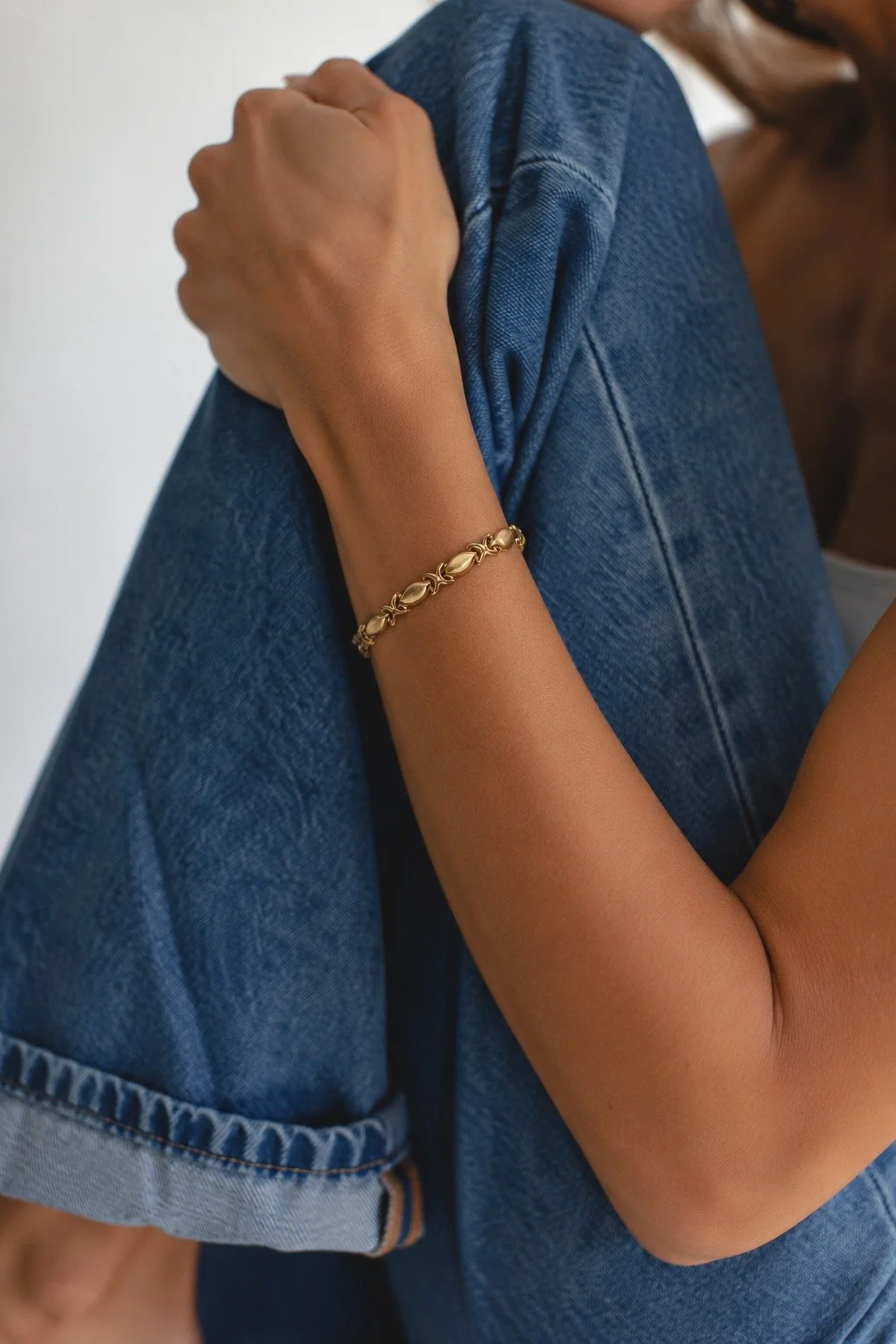 Close-up of a woman wearing a denim jacket and a gold bracelet on her wrist.
