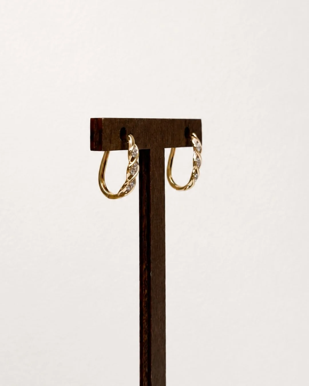 Angled view of gold twist huggie earrings with crystal accents on a wooden display stand