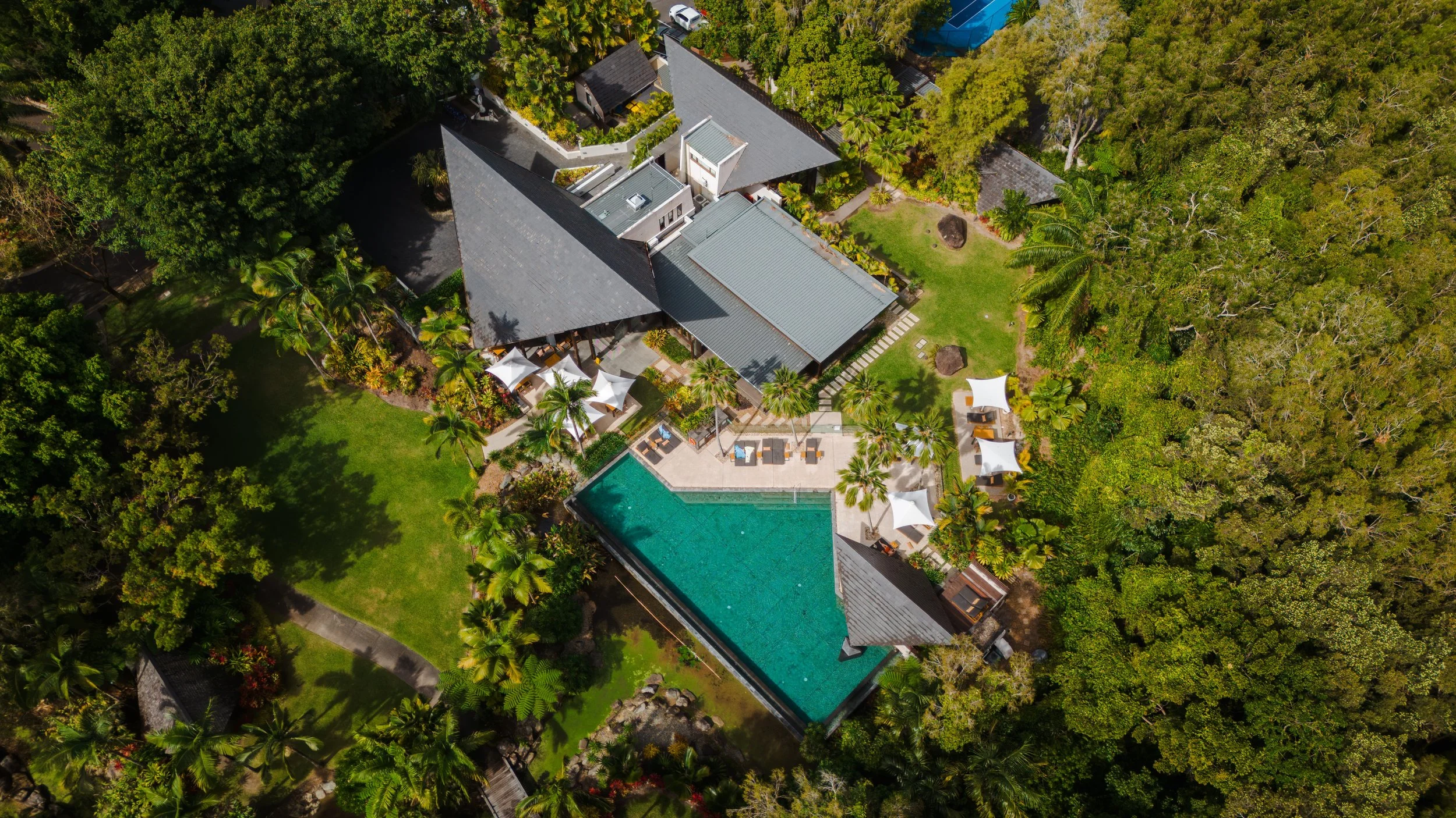 Aerial view of a large house with a swimming pool, surrounded by lush green trees and a well-maintained lawn.