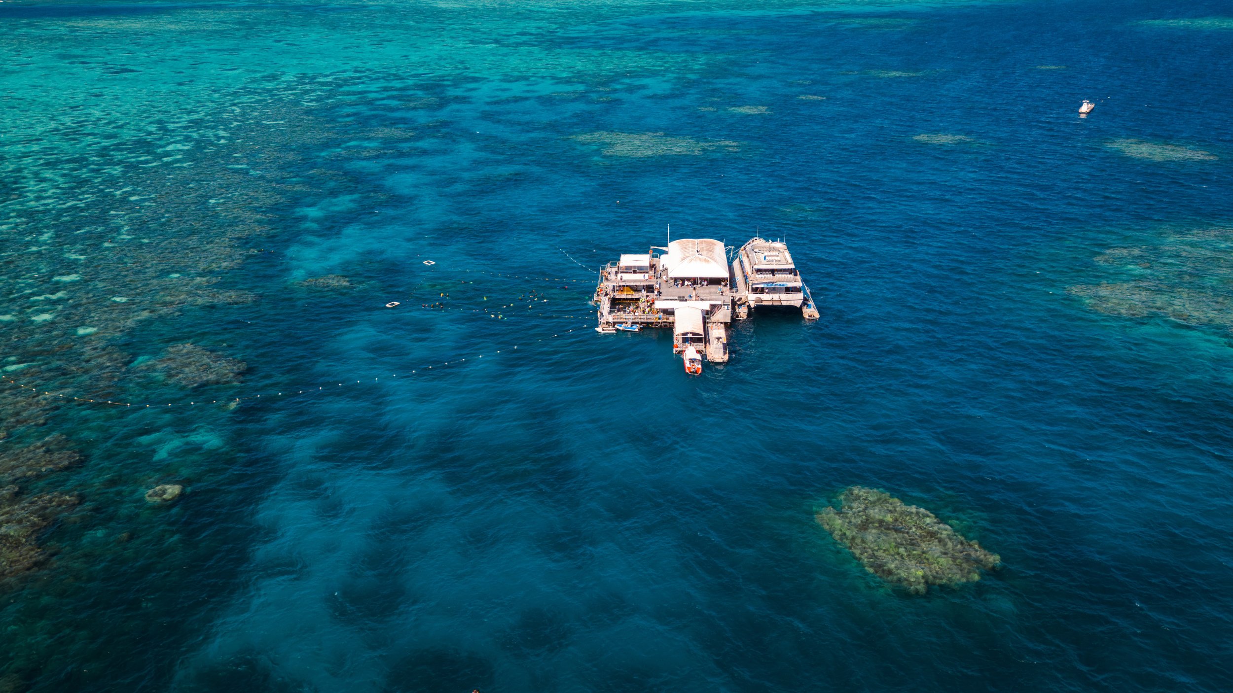 Aerial view of a marina with boats docked in clear blue water, showcasing coral reefs underneath.