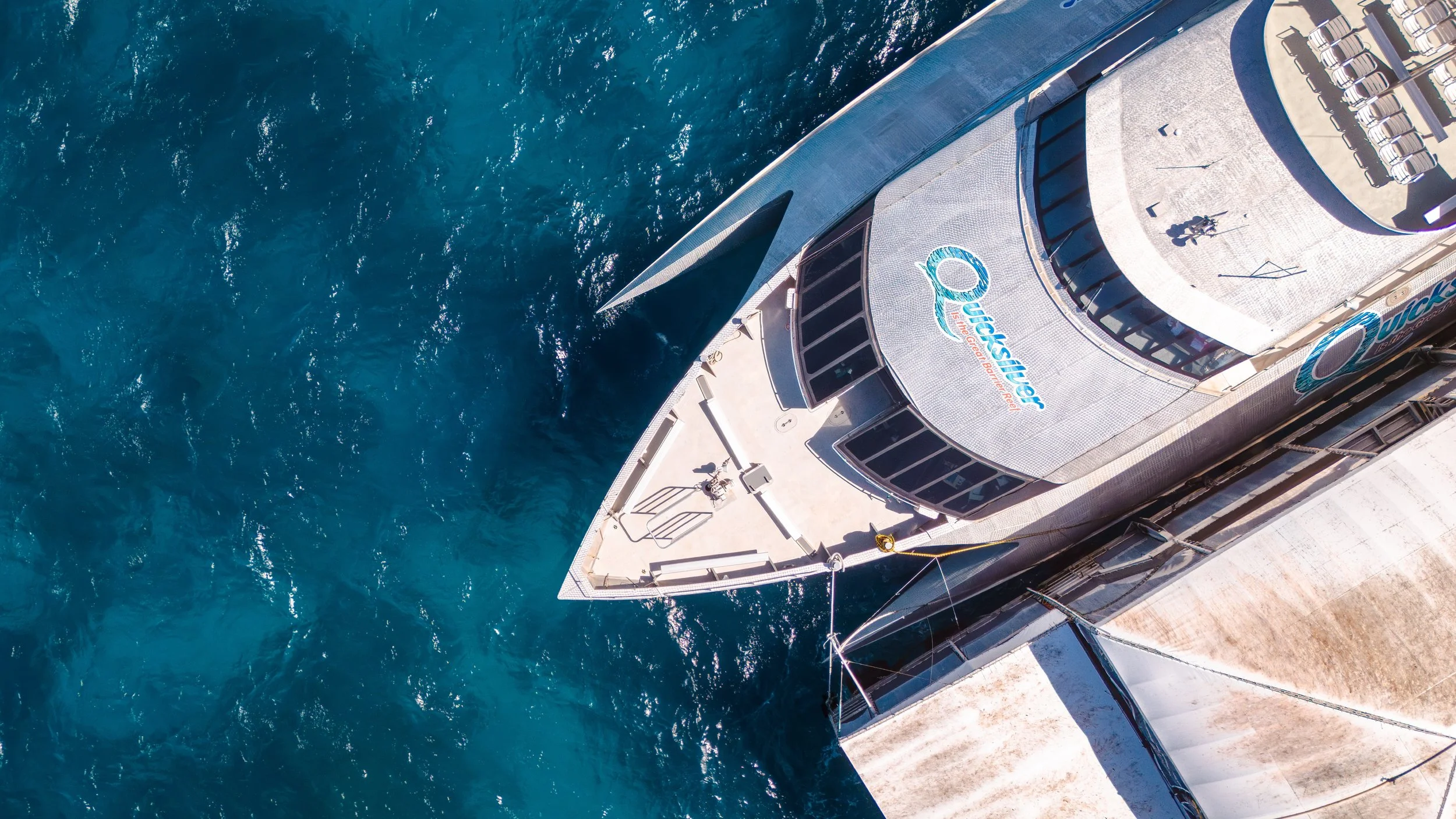 Aerial view of a docked cruise ship named 'QUEENSHER' at a port with turquoise water on one side.