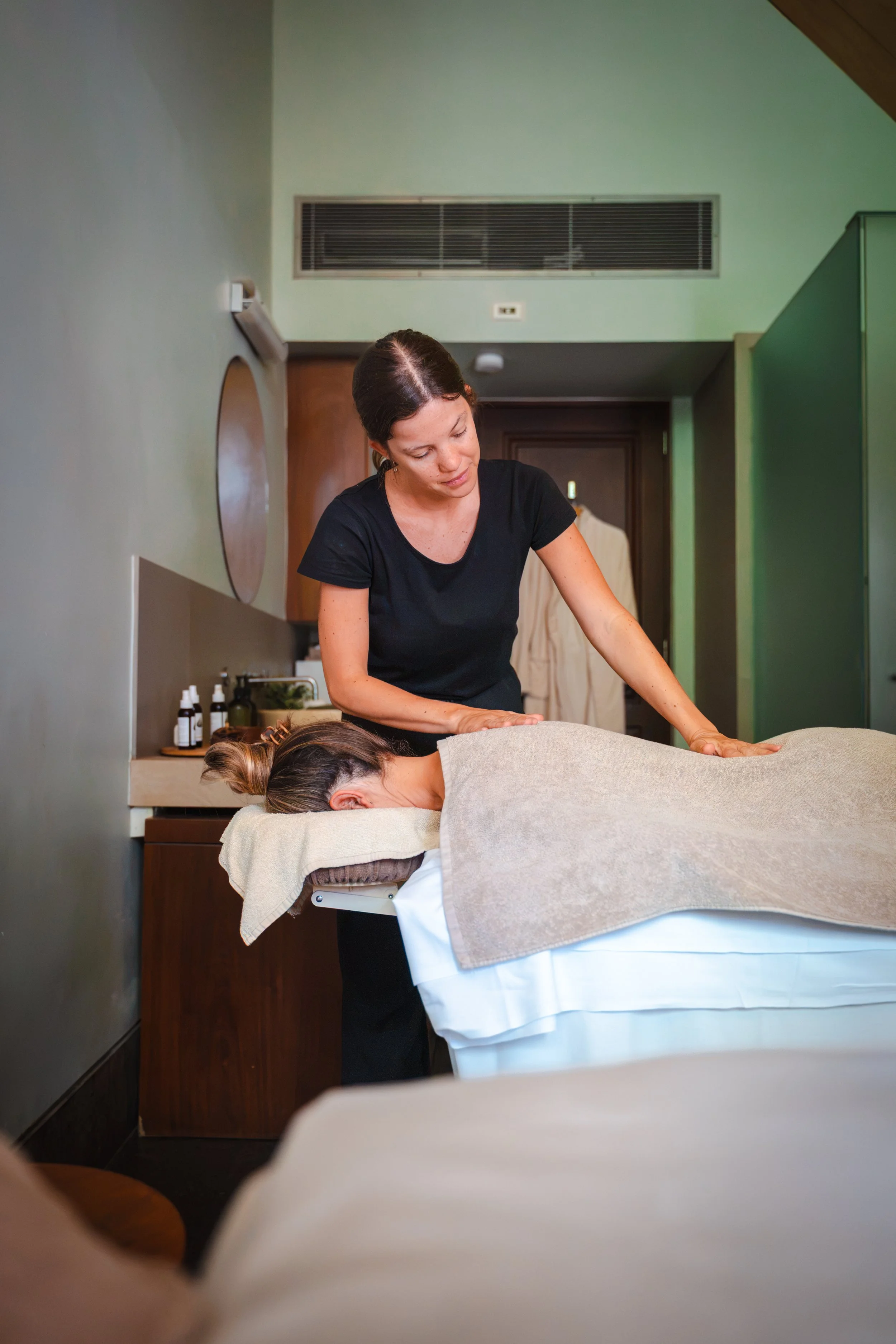A woman giving a massage to a person lying face down on a massage table in a wellness clinic room.