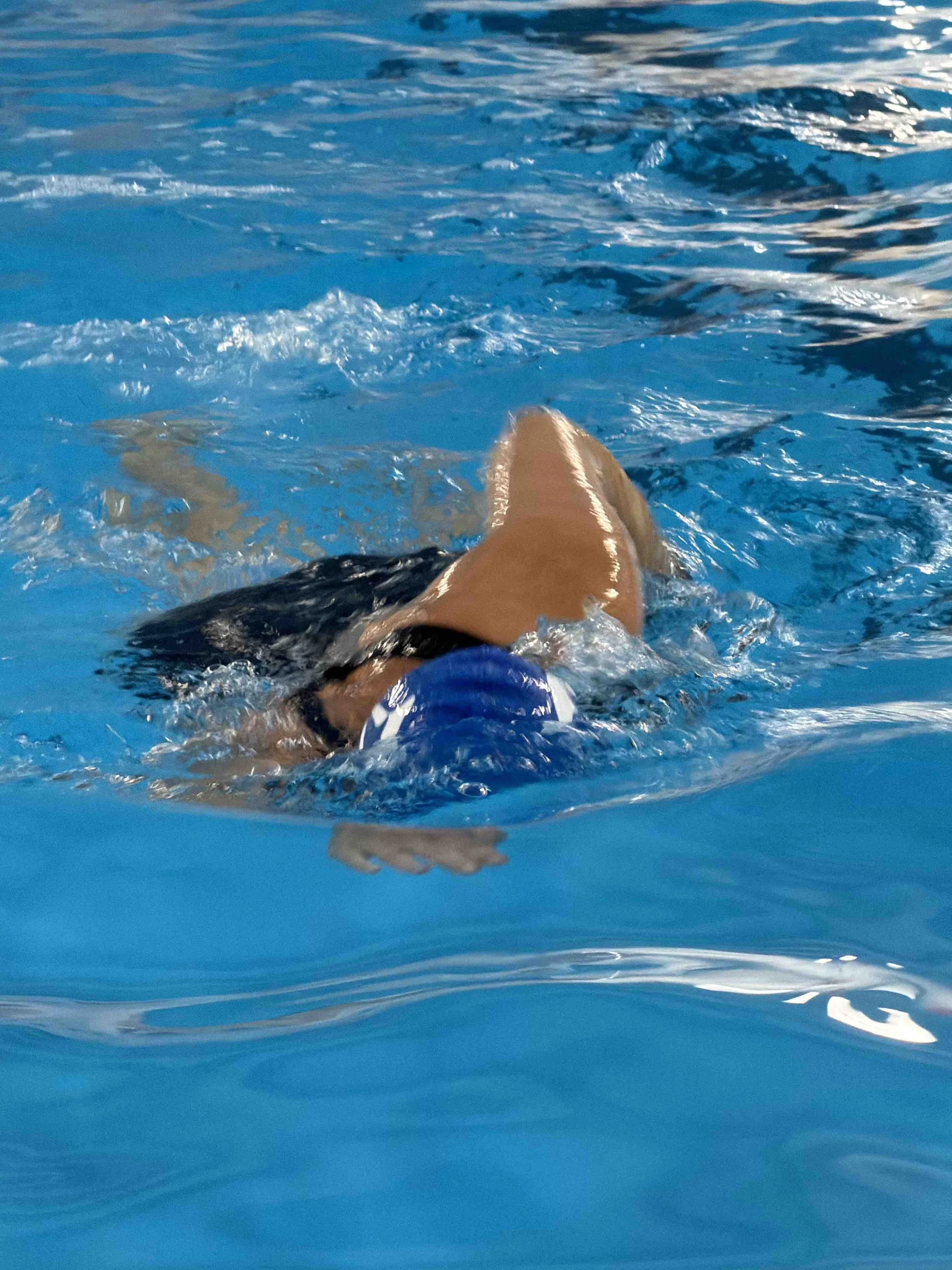 Person swimming in a pool, visible part of the swimmer's arm and head, with blue water and ripples.