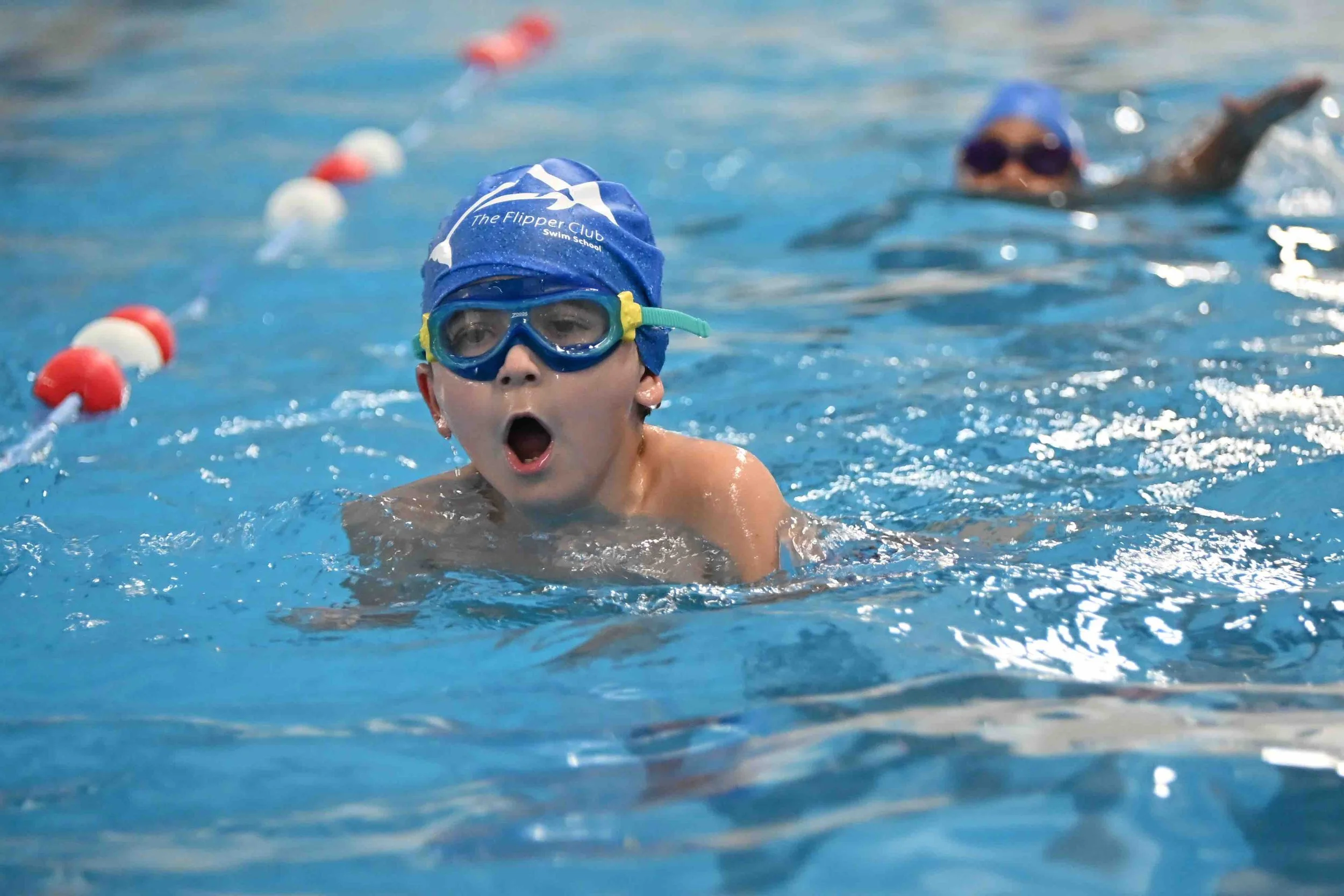 Young boy in a blue swim cap and goggles swimming in a pool during a swim lesson or practice.