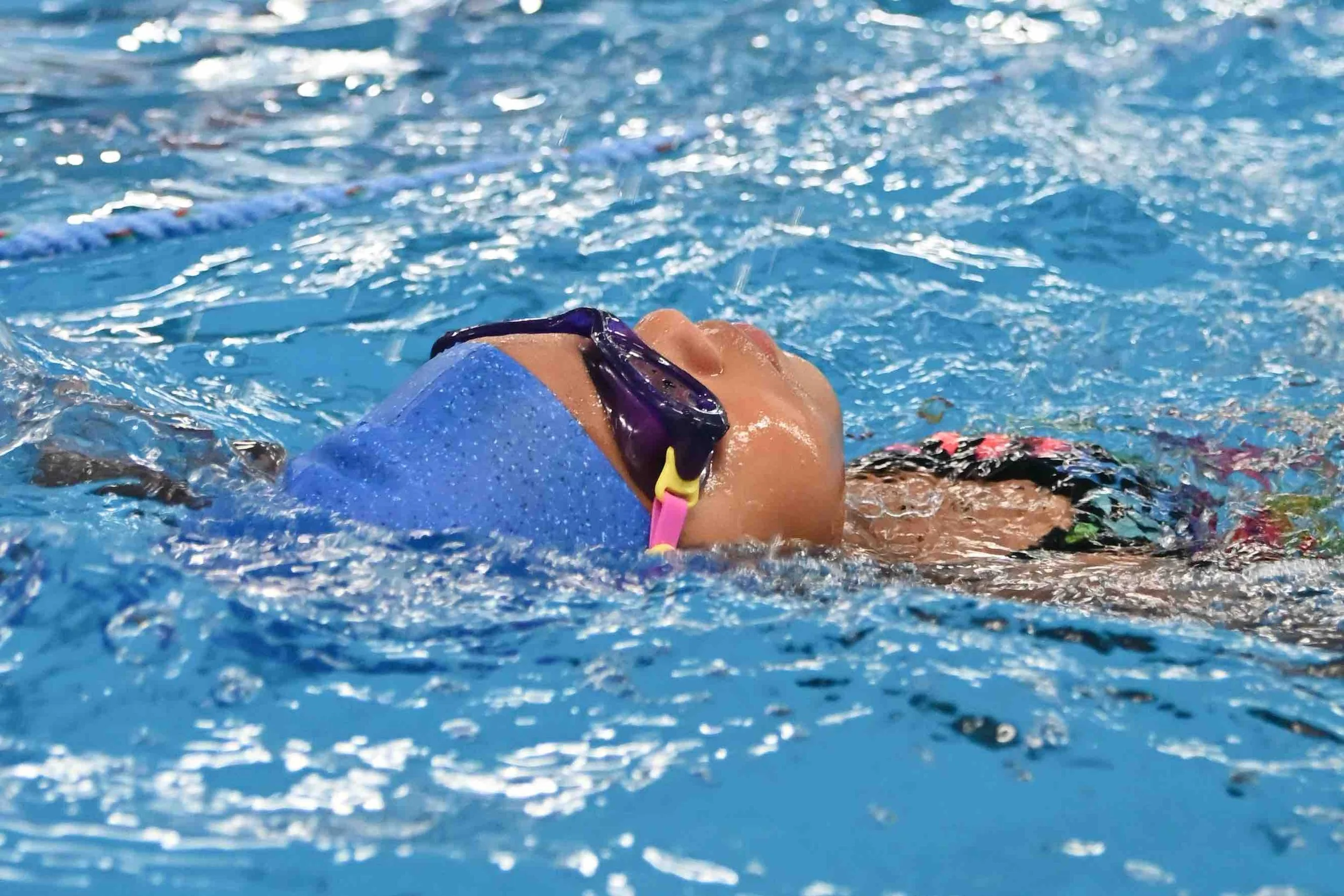Swimmer floating on back in the water wearing goggles and a swim cap.
