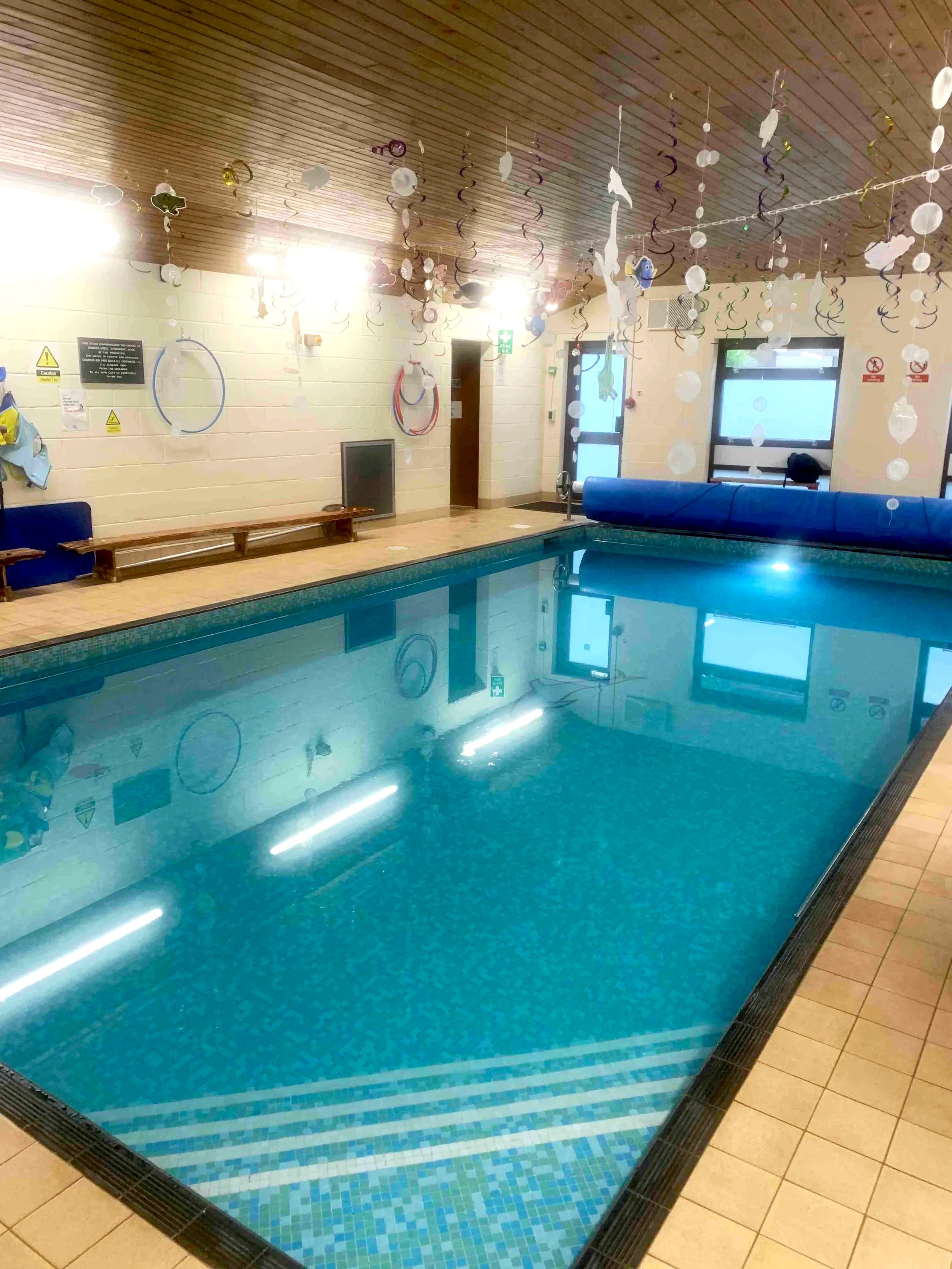 Indoor swimming pool with blue tiles, surrounded by beige tile floor, decorated with hanging paper cutouts and streamers.