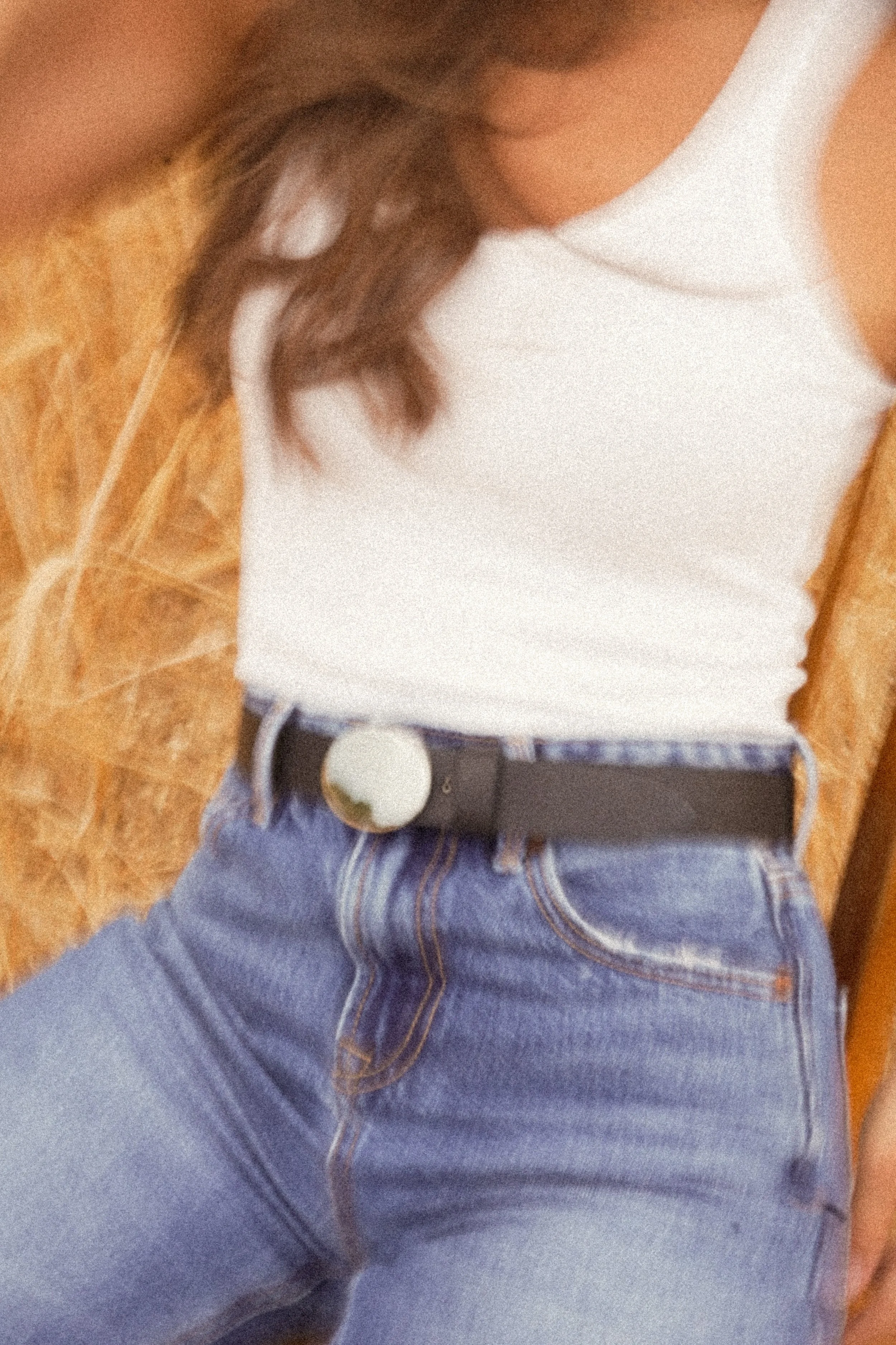Gros plan une femme portant un haut blanc, un jean bleu et une ceinture noire Atelier Nappa avec une boucle sertie d'une pierre blanche.