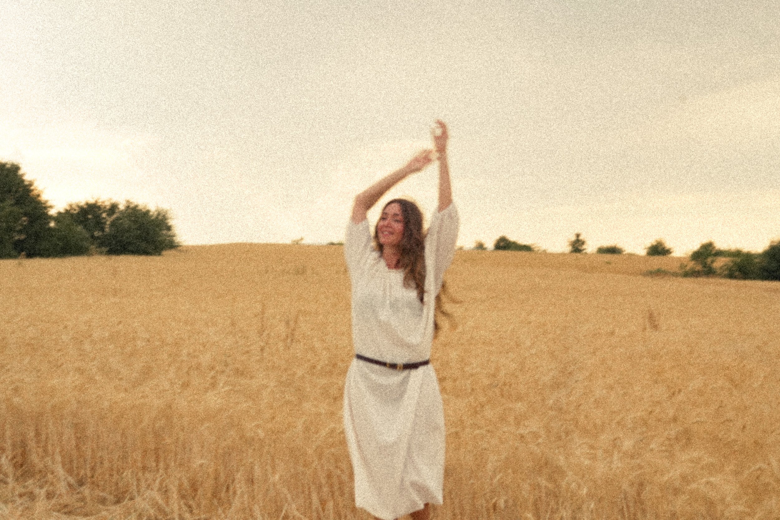 Photo d'ambiance de la marque Atelier Nappa, une femme au milieu d'un champ de blé avec une robe blanche et une ceinture en cuir marron