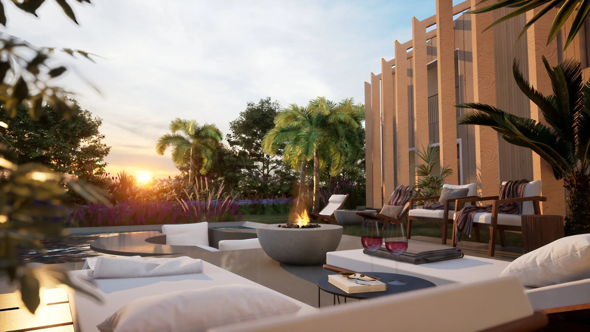 Outdoor patio with seating area, fire pit, and lush greenery including palm trees, with a modern building in the background during sunset.