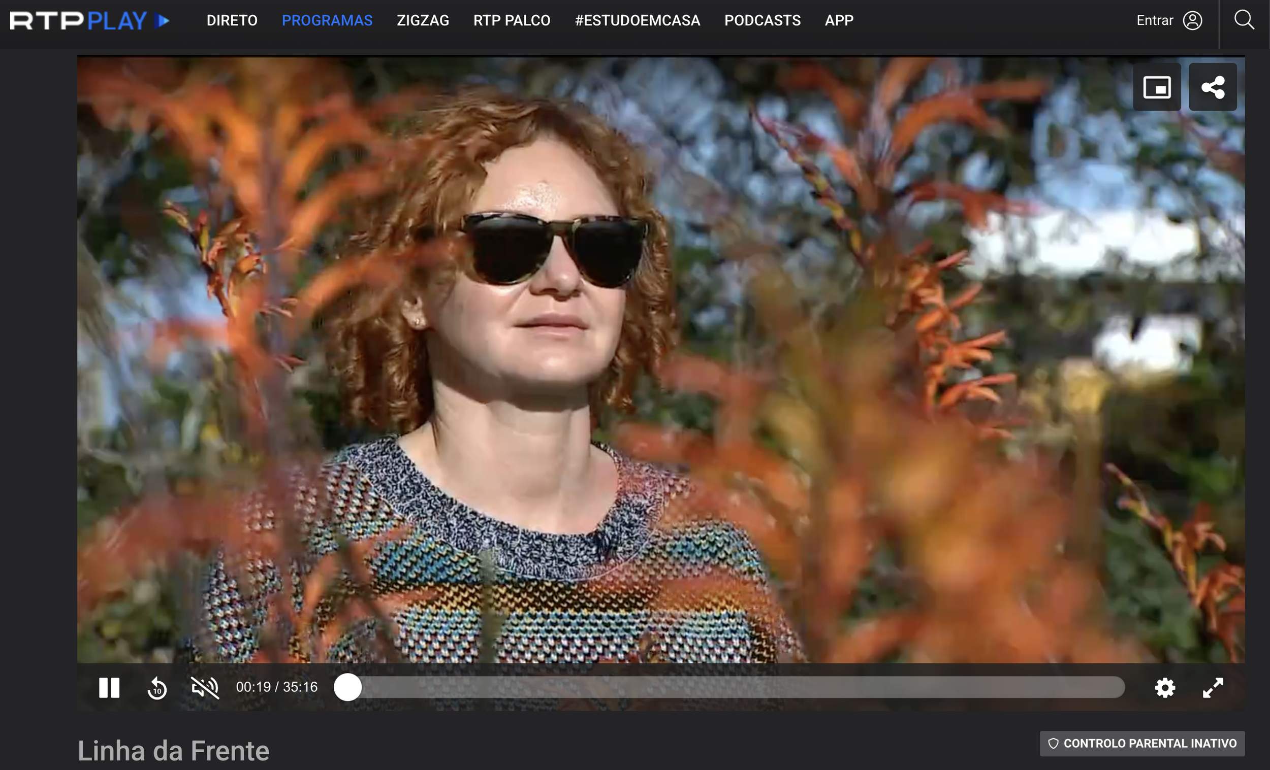 Kate Shifman filmed for Portuguese National TV on the site of AOMA Coliving, outdoors among orange and green foliage, wearing a multicolored patterned top.