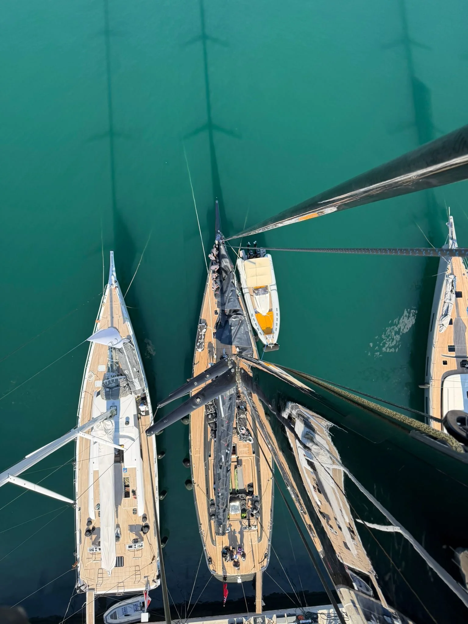 Top-down view of multiple boats docked at a marina, with calm water and reflections of the boats visible.